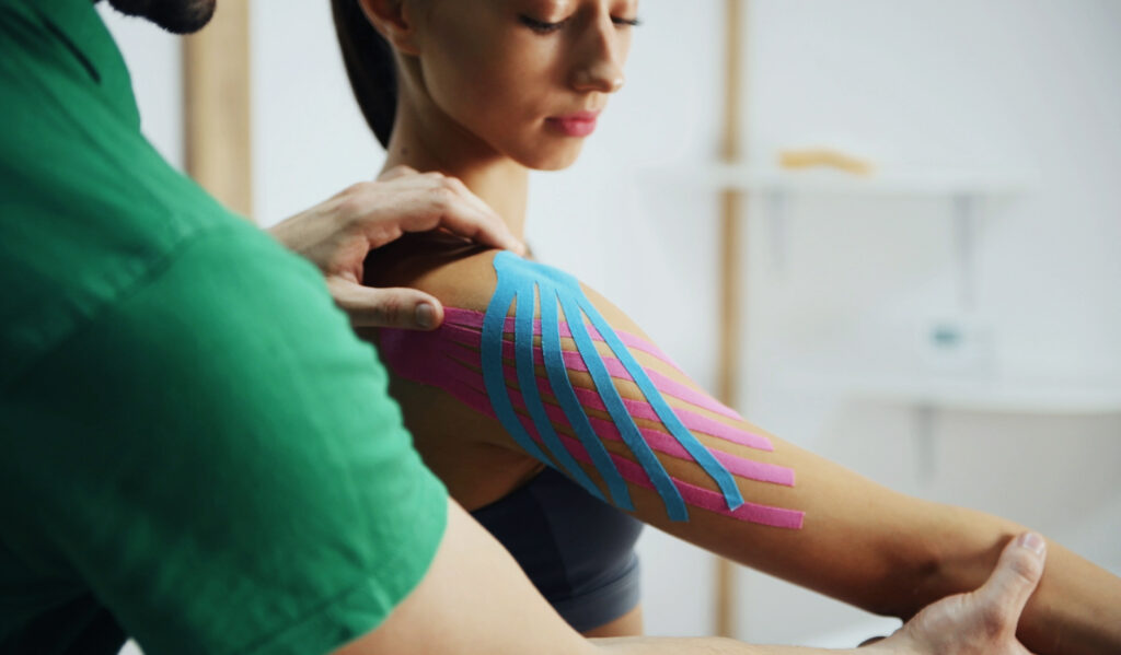 Doctor helps woman by shoulder treatment with kinesio tape.